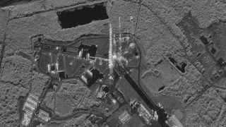 a black and white image of a rocket standing upright on a launch pad as seen from space