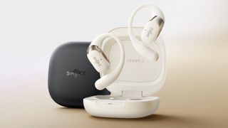 Render of the white Shokz OpenFit 2 wireless earbuds and open case, with the black, closed OpenFit 2 case sitting behind it, both in front of a faded brown background.