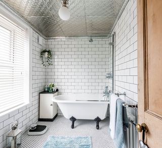bathroom with white metro tiles, patterned flooring, silver ceiling and a mini white roll top bath with black claw feet