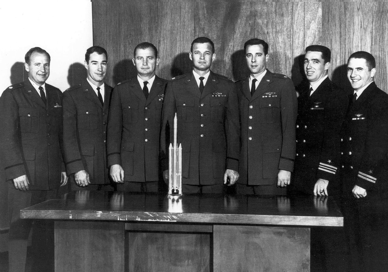 The first group of Manned Orbiting Laboratory astronauts poses in front of a model of the Titan III-M launch vehicle. Al Crews is at center.
