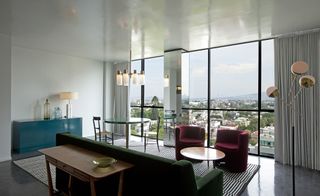 Casa Fayette dining room with large windows overlooking city, maroon tub chairs, green sofa, teal console and polished grey floors