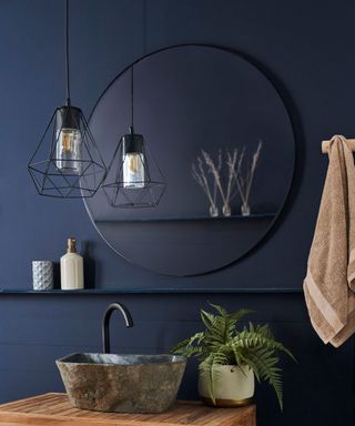 Moody dark bathroom with large round wall mirror, and caged pendant light
