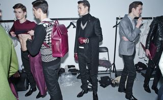 a group of men getting dressed for a show in front of clothing rails