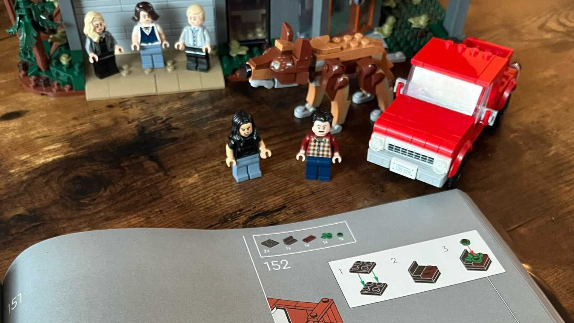 Lego The Twilight House instructions in front of minifigures, a car, wolf, and the house on a wooden table