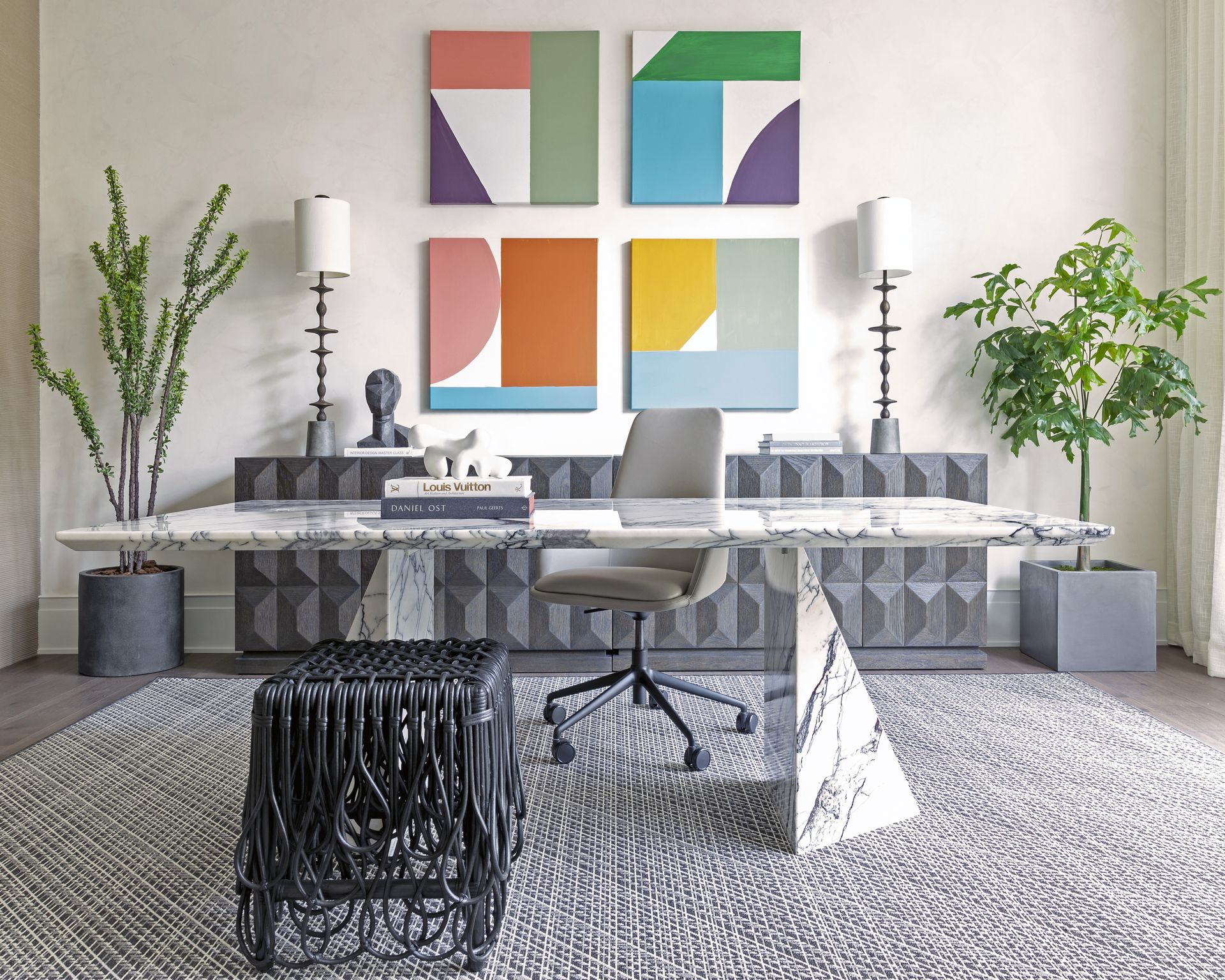 Home office with marble look desk in centre, office chair, sideboard, and abstract art on wall