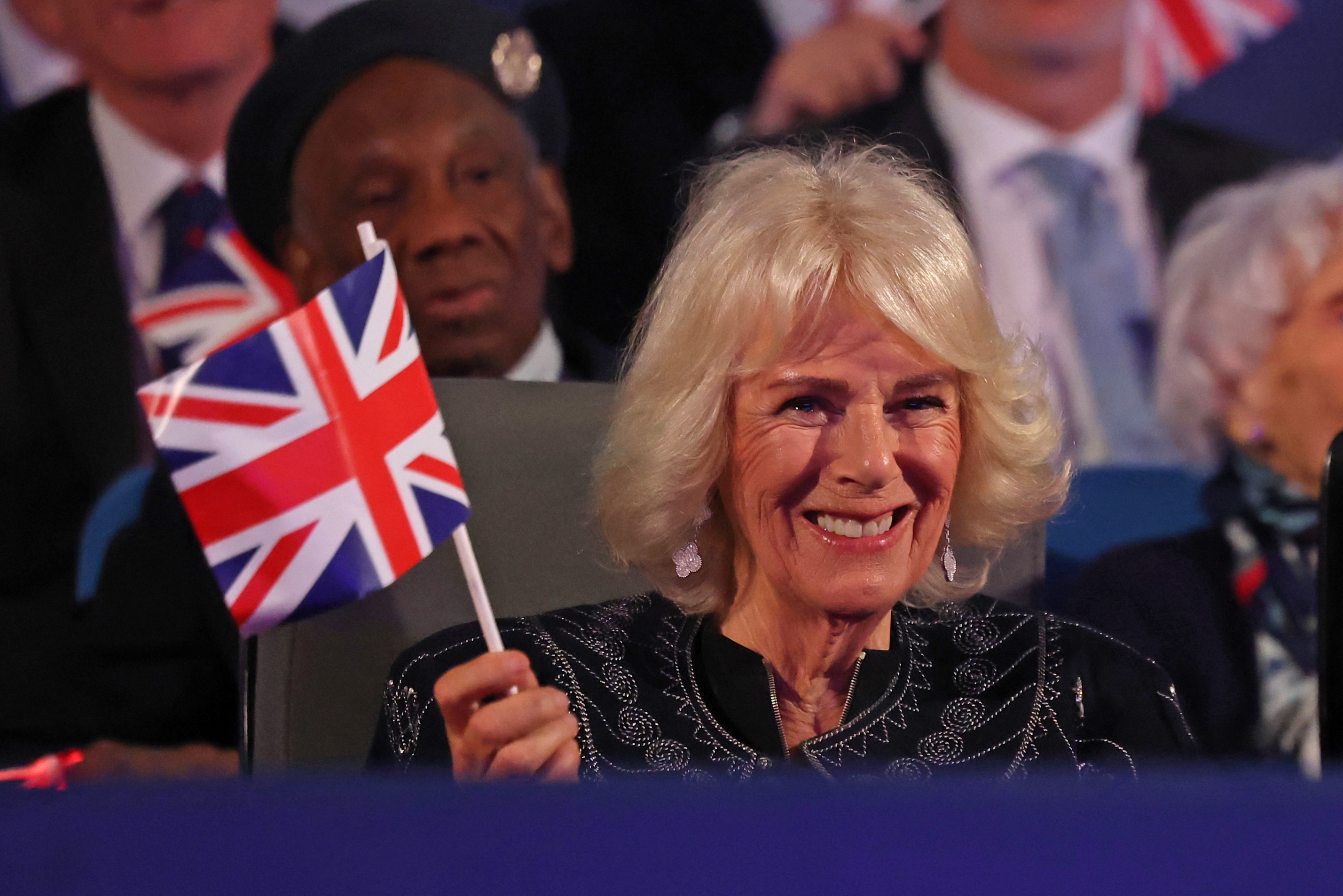 Queen Camilla waving a Union Jack and smiling