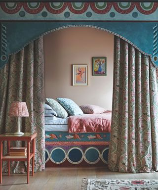 Light peach walls in bedroom with hard floors, ornate blue bed frame and framing curtain around the sleep space