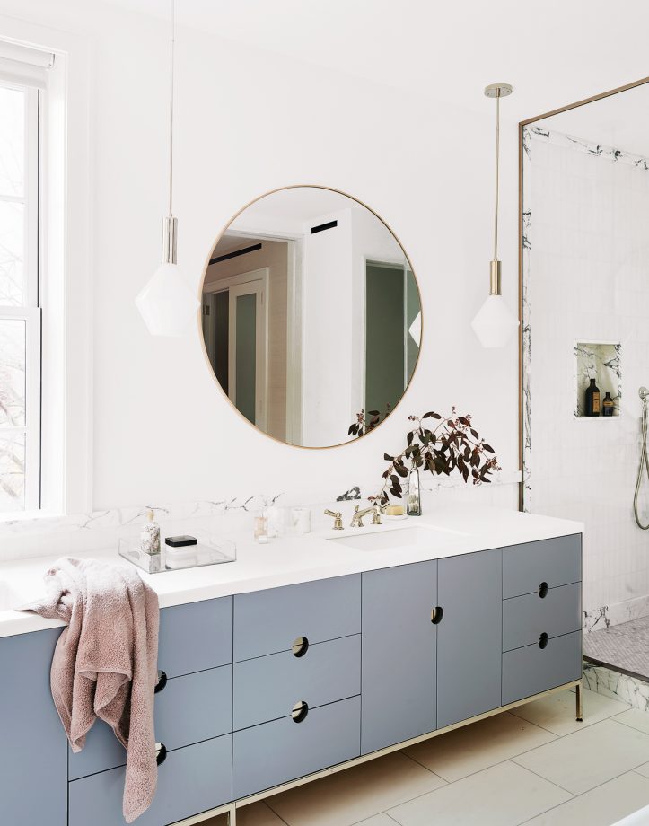 white bathroom with grey cabinetry and large round mirror