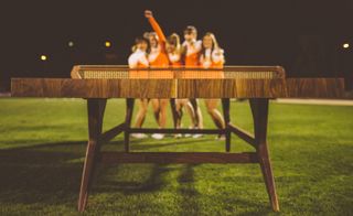 A view along the table-tennis table, to a group of five cheerleaders celebrating