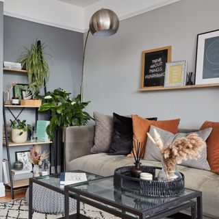 A grey-painted living room with a grey velvet sofa with multi-coloured cushions and an arched silver-finish floor lamp