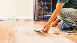 Man lifting light-coloured wooden floor plank with tool