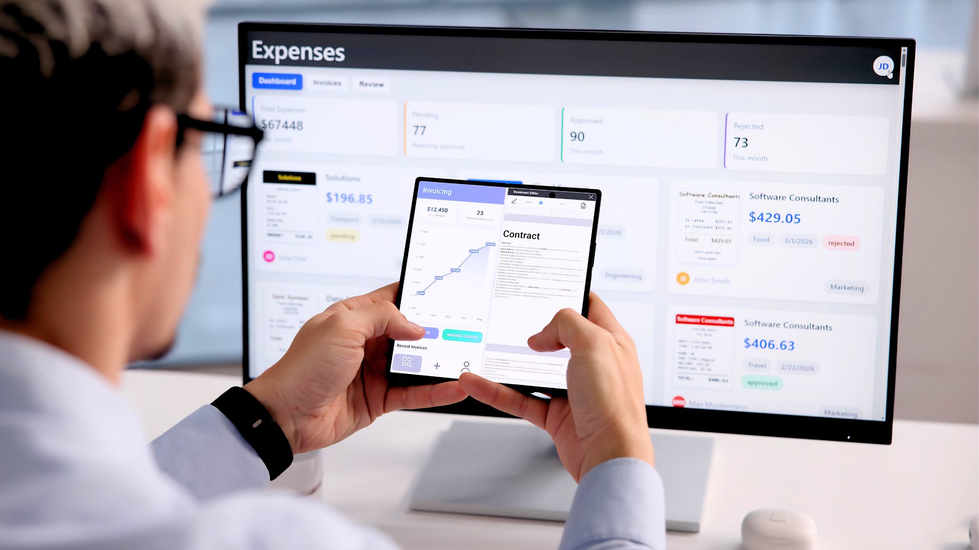 A man working on his folding phone in front of a computer screen. 