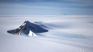 the tip of a rocky mountain rises up out of a snowy expanse