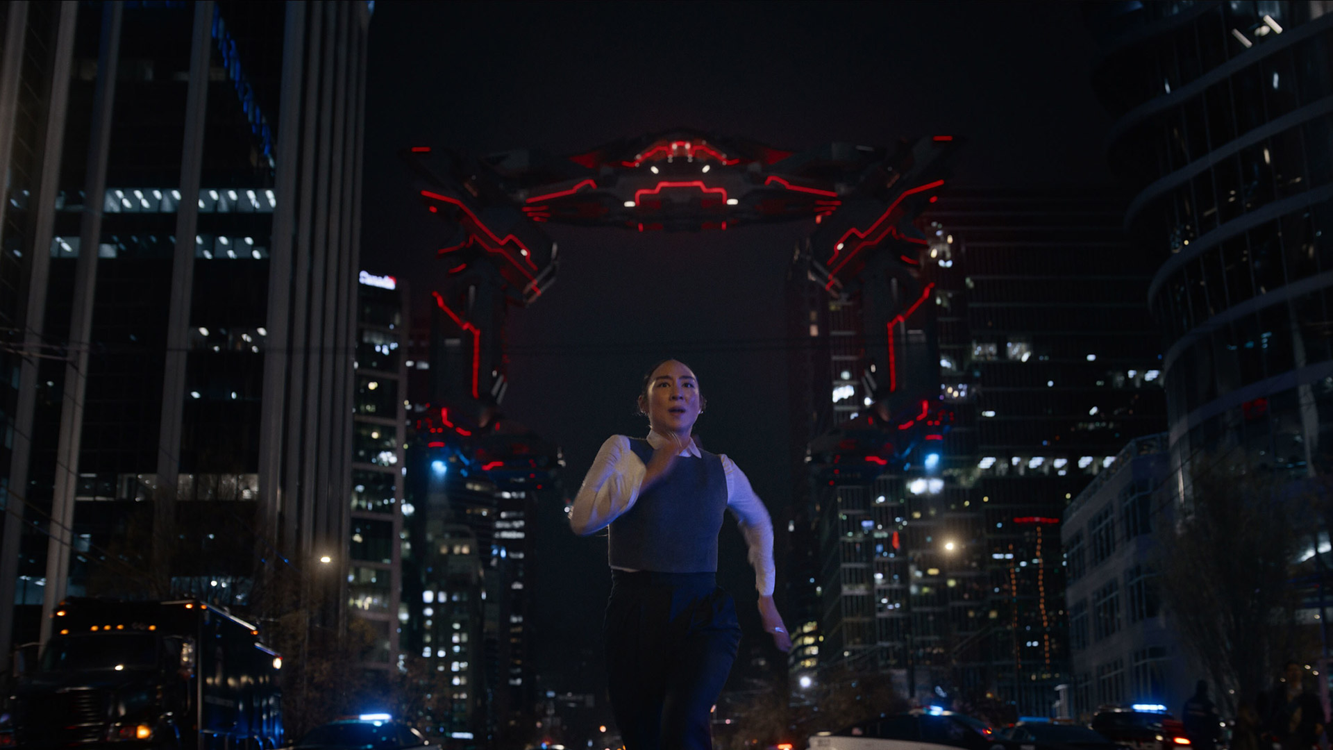 Greta Lee runs along the street of a metropolitan city with a Recognizer chasing after her