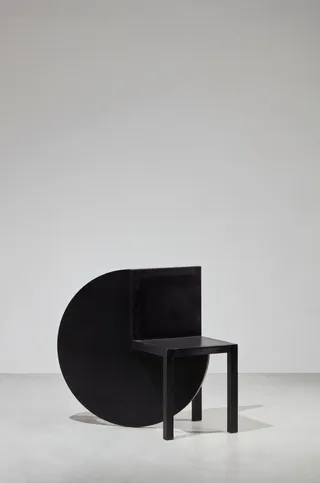 A futuristically designed chair in black wood sits in a white gallery.