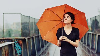Woman standing under an orange umbrella in the rain