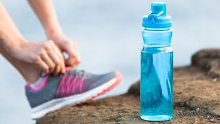Woman fastening her running shoe beside a bottle of water
