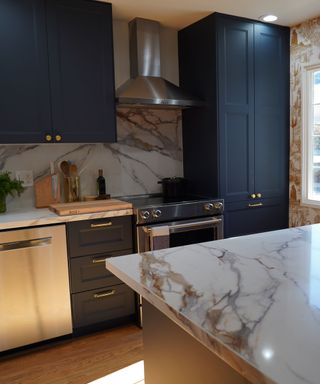 A kitchen with marble counters, a silver range hood and stove, and dark blue cabinets