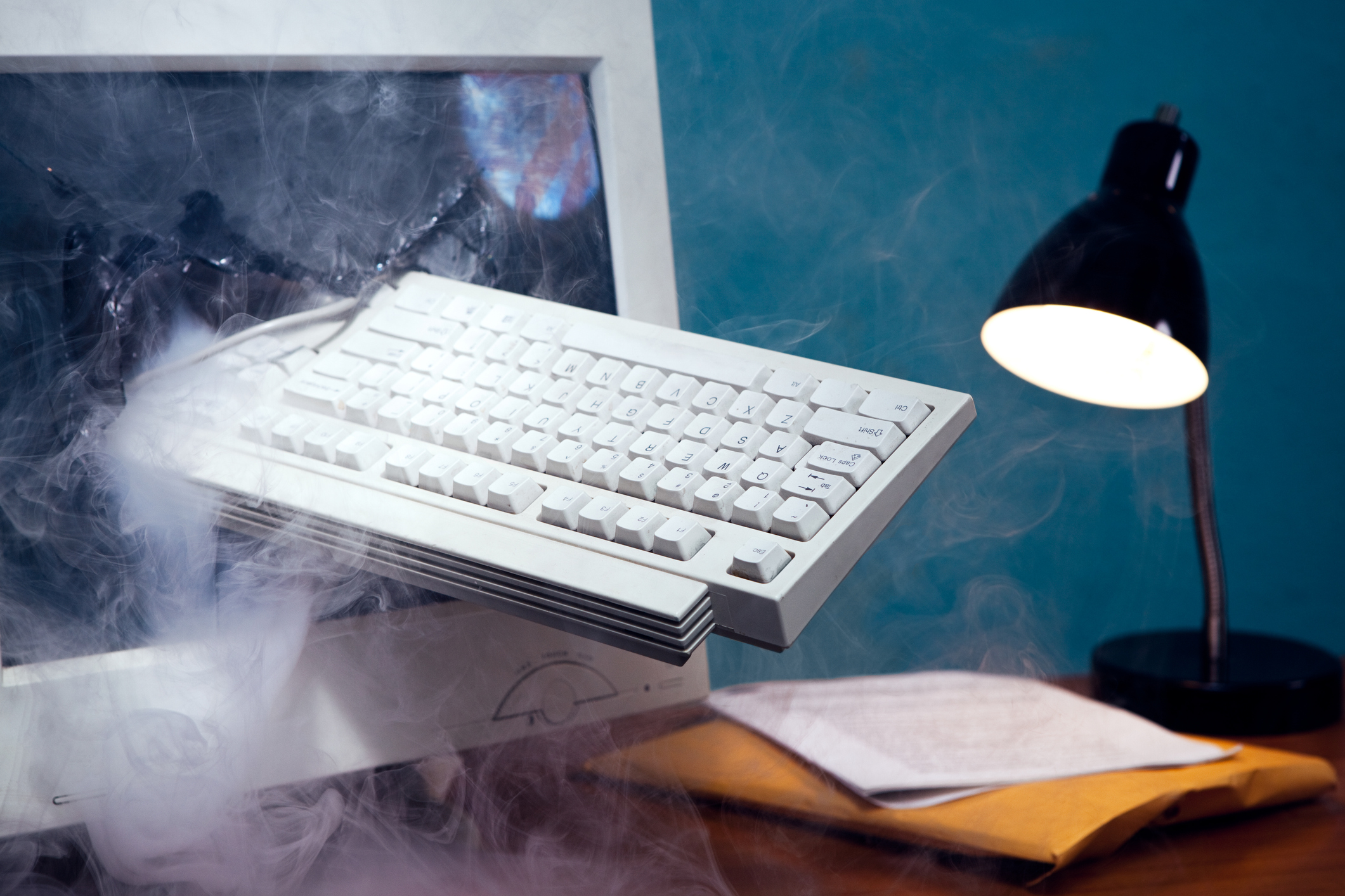 An old CRT computer monitor with a keyboard sticking out of its broken, smoking glass screen.