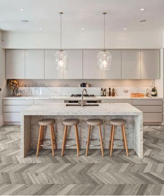 wood effect tiles in parquet herringbone pattern in a beige kitchen with island, bar stools and statement lighting