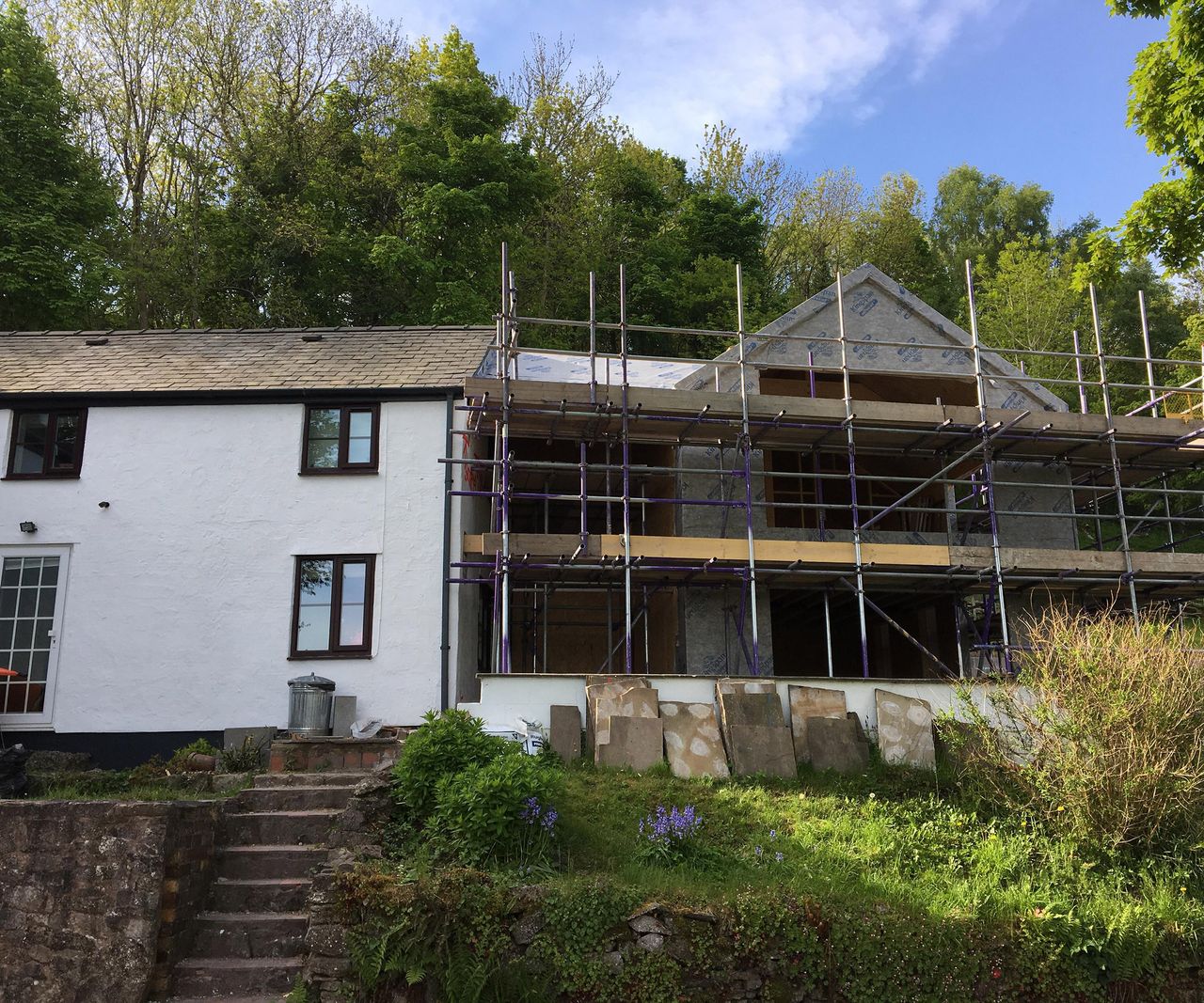 A large double-storey extension with large contemporary style glazing being built next to an existing white detached cottage