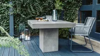 A concrete outdoor table with a woven rope chair on dark grey decking