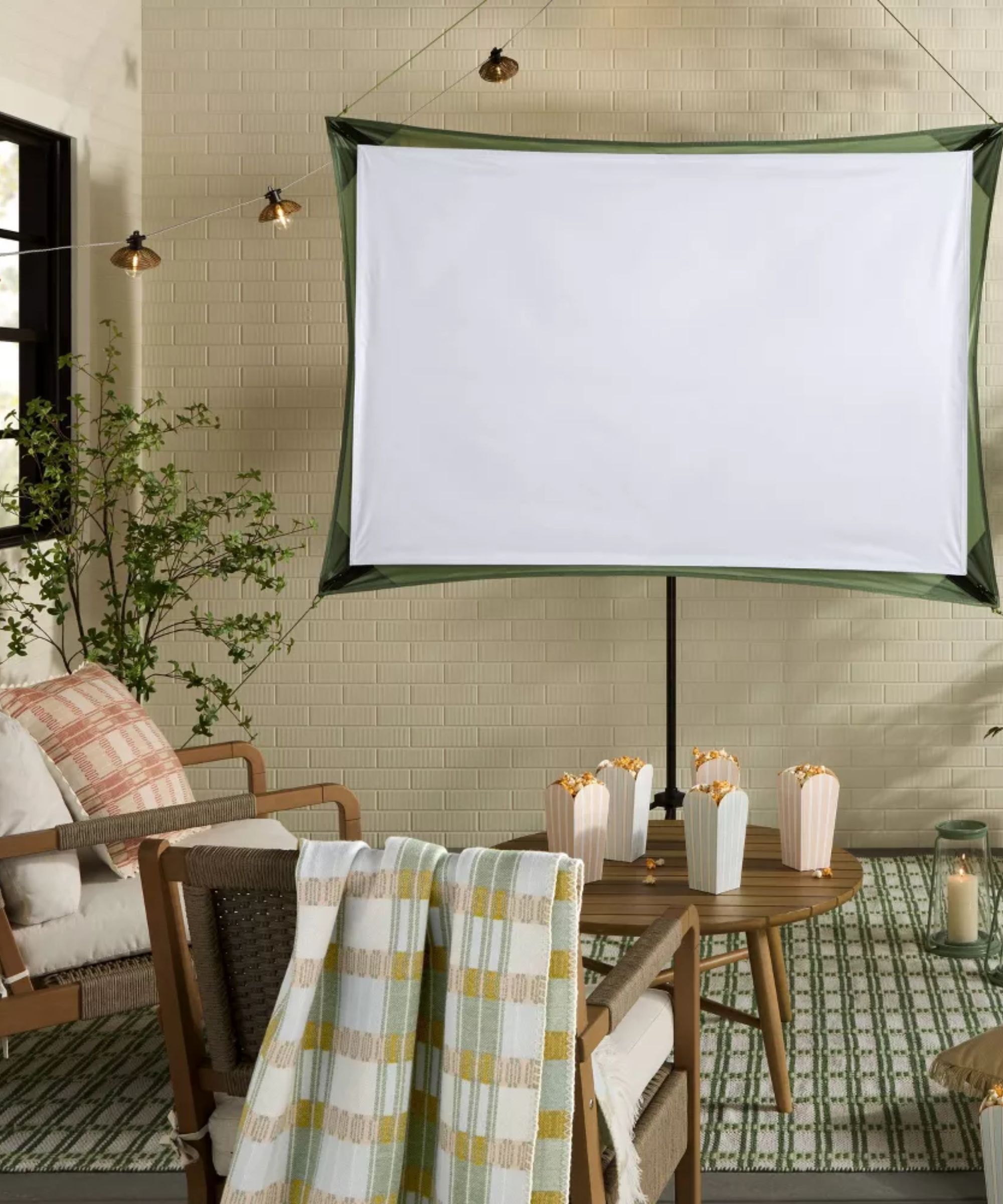 Outdoor movie night in a walled courtyard garden with wooden seats and table with cushions, blankets, popcorn and a projector screen