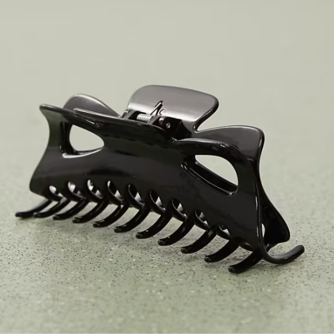 A product shot of a Weekday oversized claw hair clip in black, on a green/grey speckled background
