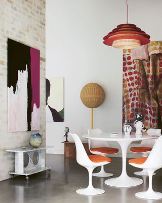 a modern dining room with tulip table and chairs, limewash brick wall, rattan floor lamp, lots of artwork