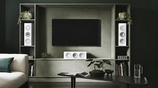The KEF R2 Meta speakers pictured on either side of a large TV in a dark living room.