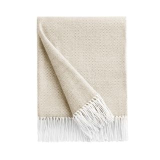 A folded beige throw blanket with white tassels