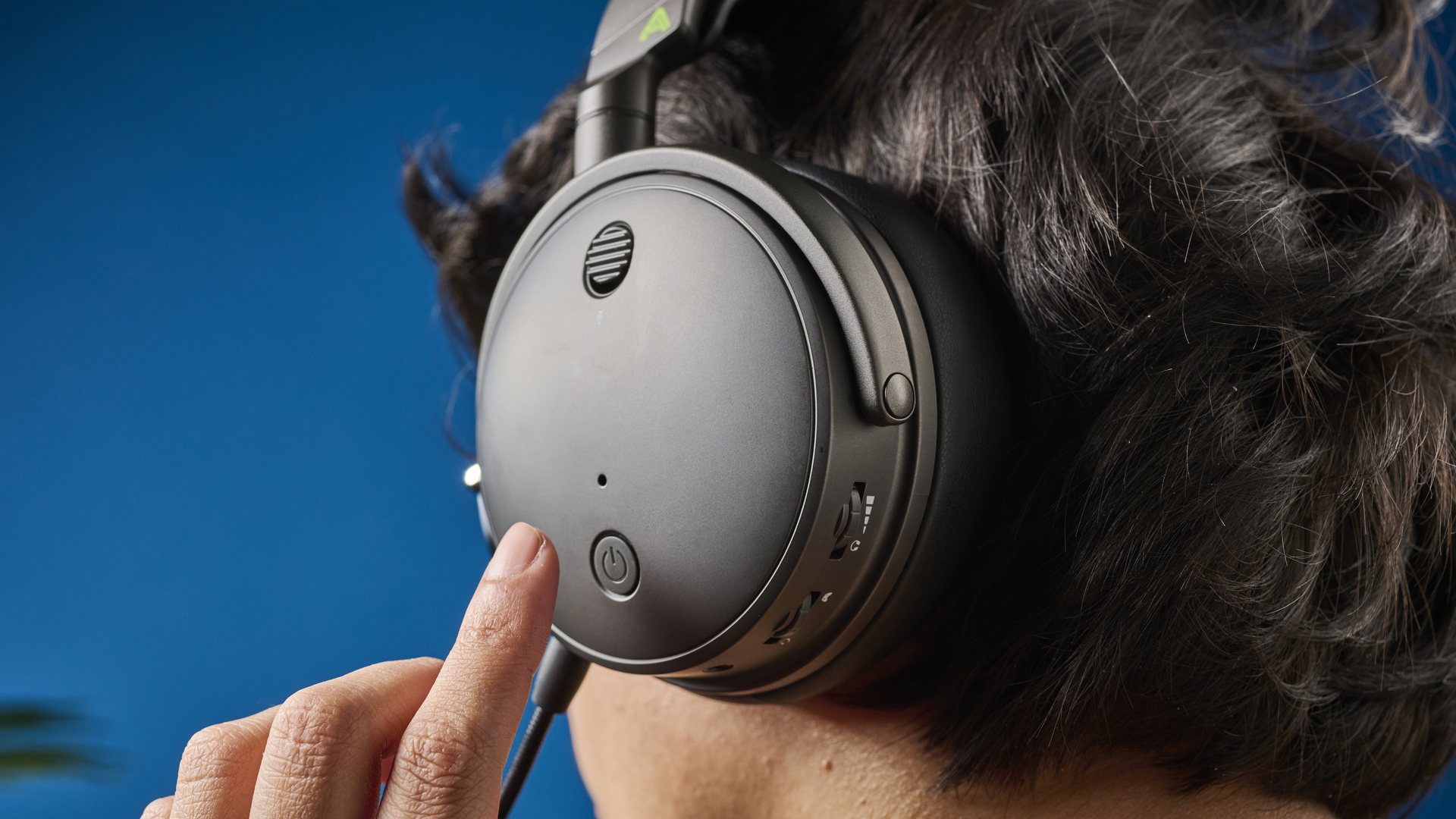 A photograph of the Audeze Maxwell on a person's head while they are touching the headset with their left hand
