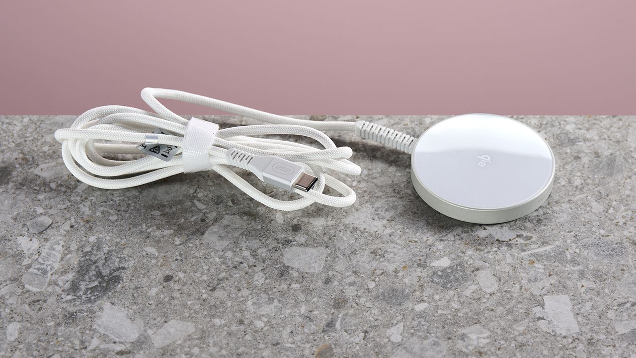 The ESR Qi2 Mini Wireless Charger sits on a light grey stone-effect surface against a pink background. The folded and secured charging cable extends from the left of the charging pad.