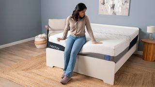 A tom's Guide tester sitting on the Nectar Luxe memory foam mattress on a bed frame in the studio