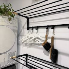 White utility room with black wall mounted clothes airers from Argos above each other on the wall next to a white tumble dryer