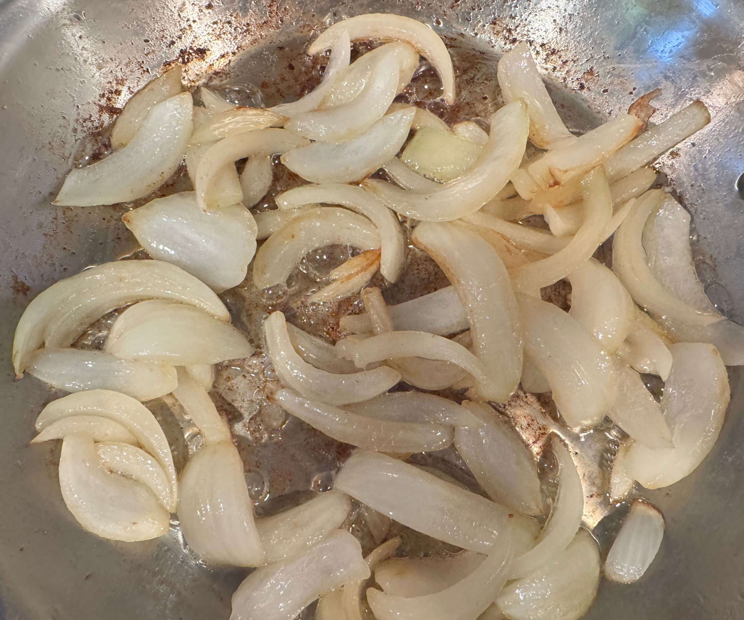 Browning chunks of onion in a stainless steel frying pan. 
