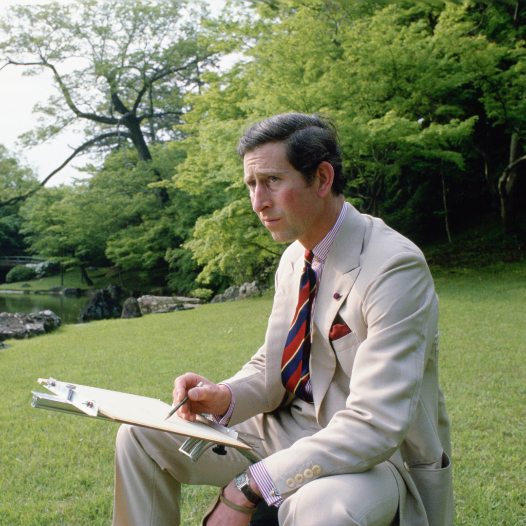A young Prince Charles sits by a lake and sketches