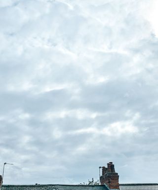 A sky with gray clouds with a dark gray roof and brick chimney underneath it