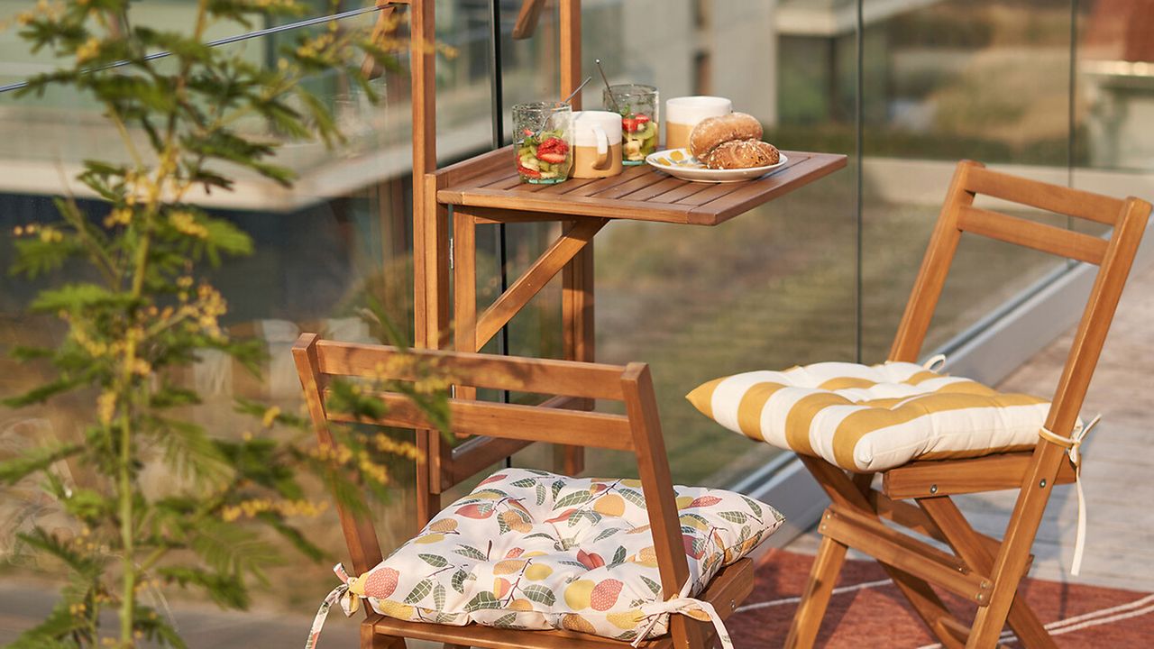 a balcony table and wooden folding chairs on a balcony with a glass balustrade