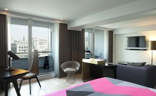 A room in the Sea Containers hotel. White walls, floor-to-ceiling windows with a terrace, a dark gray couch that looks at the tv handing on the wall, black work desk with a gray chair.