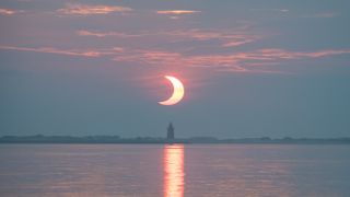 A partial solar eclipse is seen as the sun rises behind the Delaware Breakwater Lighthouse, Thursday, June 10, 2021, at Lewes Beach in Delaware. 