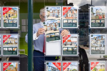 Estate agent employee placing a property for sale in the window of an estate agents