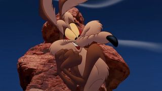 Wile E Coyote stands in front of a rock formation with a flattered expression in Looney Tunes: Back In Action.