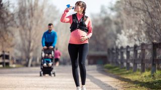 A pregnant woman stops for a drink while running