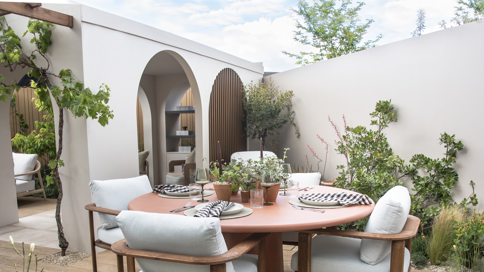 A round outdoor dining table with four chairs on a modern patio with white walls and archways