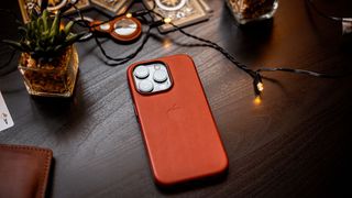 iPhone 14 in leather case on a dark wooden desk surrounded by fairy lights