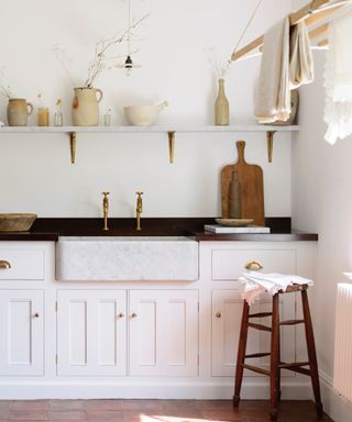 white pantry with white walls and cabinetry, black countertop, open shelving, artisan ceramics and wooden boards, wood stool, hanging dryer, deVOL