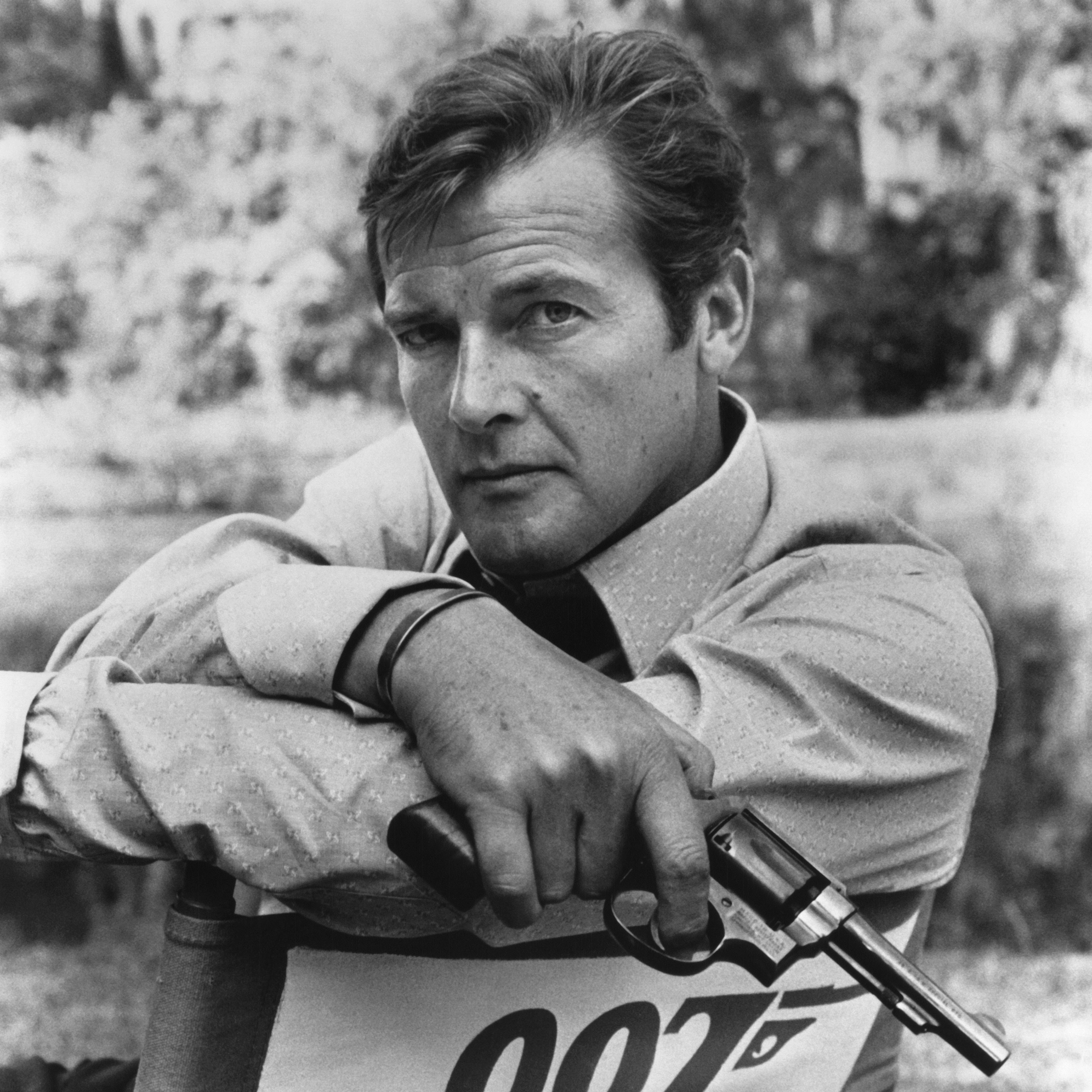 Roger Moore poses in director's chair with 007 logo holding gun as James Bond in a publicity portrait for the 1973 film 'Live and Let Die'. (Photo by Screen Archives/Getty Images)
