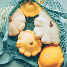 Five yellow and white pattypan squash in a blue string bag