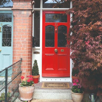 A front porch with a red front door and potted plants around it
